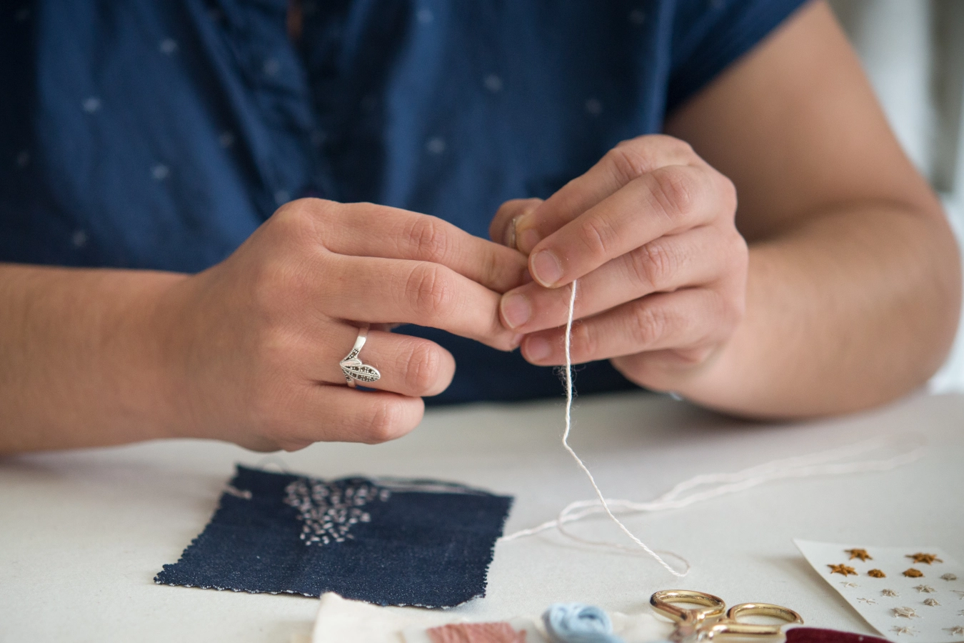 manos enhebrando aguja fondo azul